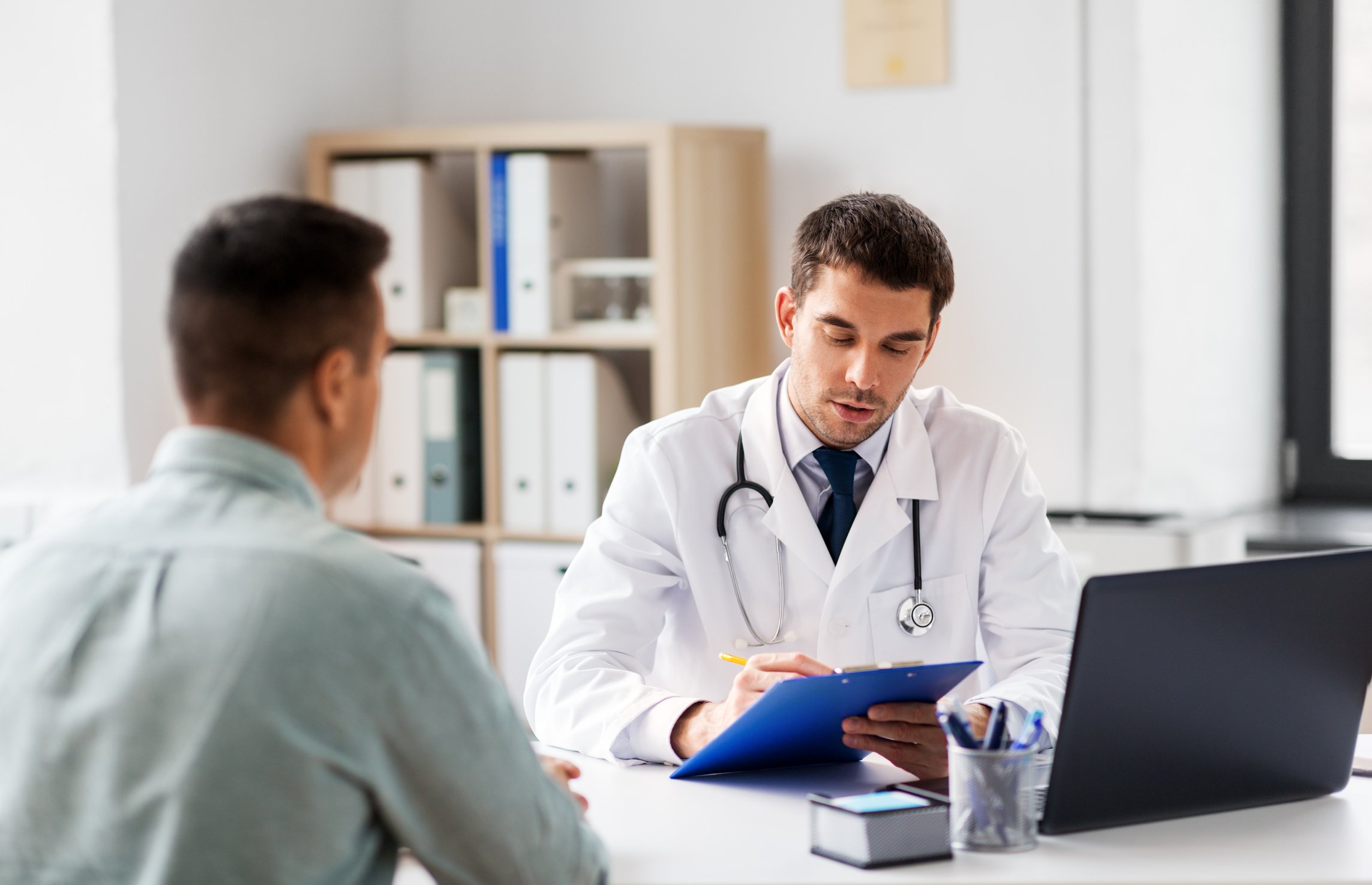 Doctor with Clipboard and Male Patient at Hospital